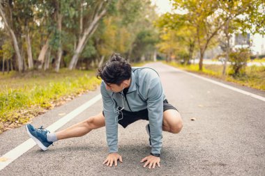 Genç adam koşmadan önce parkta geriniyor. Genç adam parktaki fitness antrenmanından önce antrenman yapıyor. Sağlıklı ve egzersiz yapan genç adam ormanın yanındaki yolda ısınıyor..
