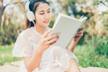 Kulaklıklı bir kız müzik dinler ve ormanda roman okur. hobi ve piknik konsepti.