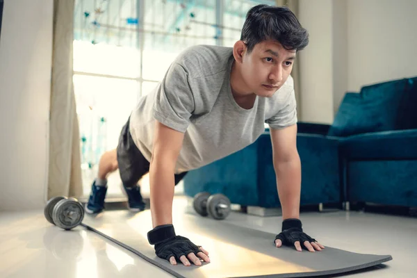 Young man doing push up and exercises on yoga mat in living room at home. Fitness, workout and traning at home concept.