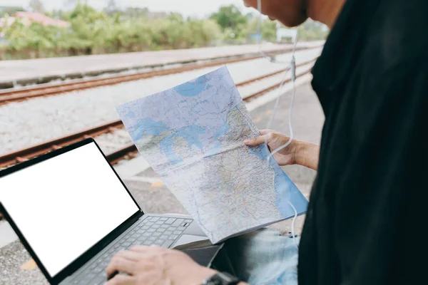 Young asian man using laptop and check map for working and search location for travel at train station. Freelance work and travel concept.