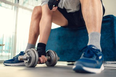 Evdeki oturma odasında, halterli halterle yoga minderi üzerinde egzersiz yapan genç adam. Spor, spor ve ev konseptinde geçiş.