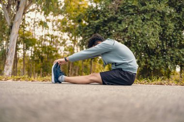 Genç adam koşmadan önce parkta geriniyor. Genç adam parktaki fitness antrenmanından önce antrenman yapıyor. Sağlıklı ve egzersiz yapan genç adam ormanın yanındaki yolda ısınıyor..