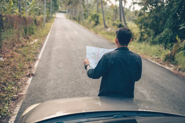A man with backpack hiking read a map in front of car on the road in forest. Backpack travel concept.