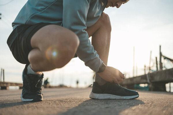 closeup of man tying shoe laces on the road before running in sunset. Sport and workout concept.