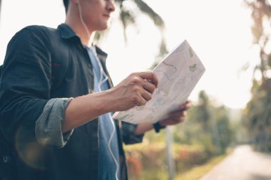 Sırt çantalı bir adam harita okuyor ve ormanda yolda yürüyor. Sırt çantası seyahat kavramı.