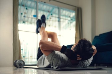 Genç adam evdeki oturma odasında yoga minderi üzerinde abdominal egzersizler yapıyor. Spor, spor ve ev konseptinde geçiş.