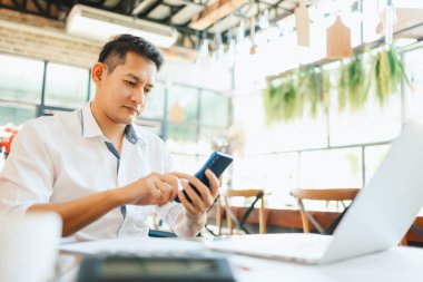 İş yerinde çalışan ve akıllı telefon ve defter bilgisayarı kullanan genç işadamı