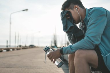Spor adamı koşudan sonra dinleniyor ve terini havluyla ve su şişesiyle siliyor. spor ve egzersiz konsepti.