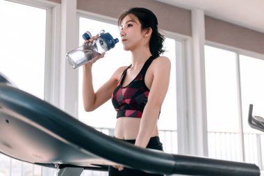 Kadın spor salonunda koşu bandında su içiyor..