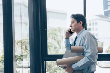 Meşgul işadamı cep telefonu kullanıyor ve elleri dosya ve çizim tüpü tutuyor. Yoğun ya da yapacak çok iş var, adam iş kavramını vurguladı.