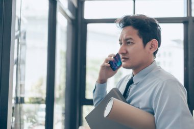 Meşgul işadamı cep telefonu kullanıyor ve elleri dosya ve çizim tüpü tutuyor. Yoğun ya da yapacak çok iş var, adam iş kavramını vurguladı.