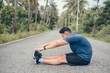 Genç adam koşmadan önce parkta geriniyor. Genç adam parktaki fitness antrenmanından önce antrenman yapıyor. Sağlıklı ve egzersiz yapan genç adam ormanda ısınıyor..