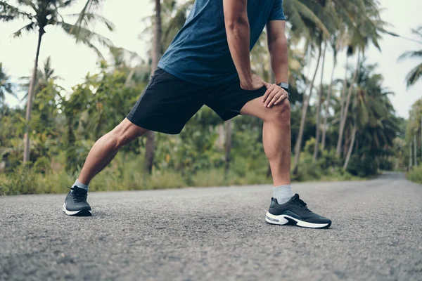 Genç adam koşmadan önce parkta geriniyor. Genç adam parktaki fitness antrenmanından önce antrenman yapıyor. Sağlıklı ve egzersiz yapan genç adam ormanda ısınıyor..