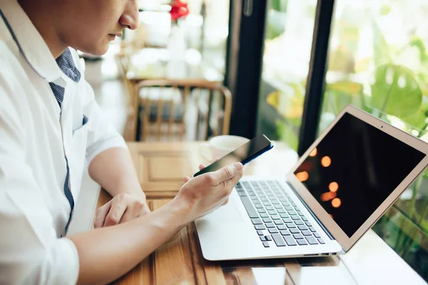 İş yerinde çalışan ve akıllı telefon ve defter bilgisayarı kullanan genç işadamı