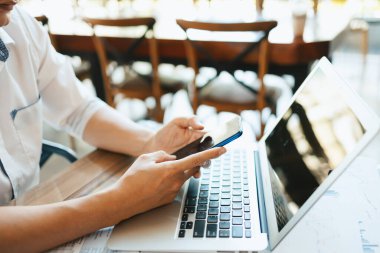 İş yerinde çalışan ve akıllı telefon ve defter bilgisayarı kullanan genç işadamı
