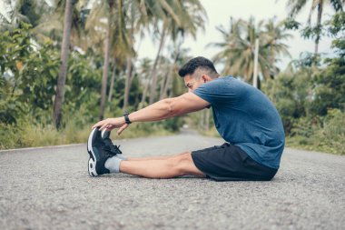 Genç adam koşmadan önce parkta geriniyor. Genç adam parktaki fitness antrenmanından önce antrenman yapıyor. Sağlıklı ve egzersiz yapan genç adam ormanda ısınıyor..