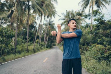 Genç adam koşmadan önce parkta geriniyor. Genç adam parktaki fitness antrenmanından önce antrenman yapıyor. Sağlıklı ve egzersiz yapan genç adam ormanda ısınıyor..