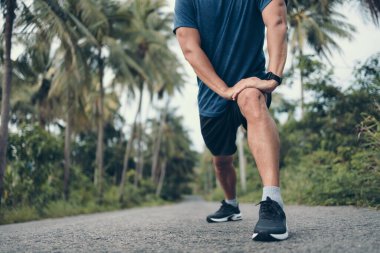 Genç adam koşmadan önce parkta geriniyor. Genç adam parktaki fitness antrenmanından önce antrenman yapıyor. Sağlıklı ve egzersiz yapan genç adam ormanda ısınıyor..