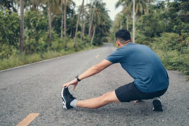 Genç adam koşmadan önce parkta geriniyor. Genç adam parktaki fitness antrenmanından önce antrenman yapıyor. Sağlıklı ve egzersiz yapan genç adam ormanda ısınıyor..