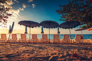Güneş şemsiyeleri ve plajda gün batımlı plaj sandalyeleri..
