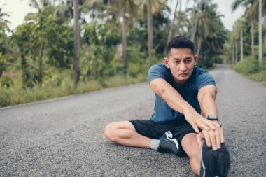 Genç adam koşmadan önce parkta geriniyor. Genç adam parktaki fitness antrenmanından önce antrenman yapıyor. Sağlıklı ve egzersiz yapan genç adam ormanda ısınıyor..