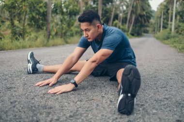 Genç adam koşmadan önce parkta geriniyor. Genç adam parktaki fitness antrenmanından önce antrenman yapıyor. Sağlıklı ve egzersiz yapan genç adam ormanda ısınıyor..