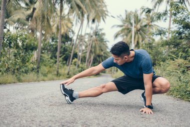Genç adam koşmadan önce parkta geriniyor. Genç adam parktaki fitness antrenmanından önce antrenman yapıyor. Sağlıklı ve egzersiz yapan genç adam ormanda ısınıyor..