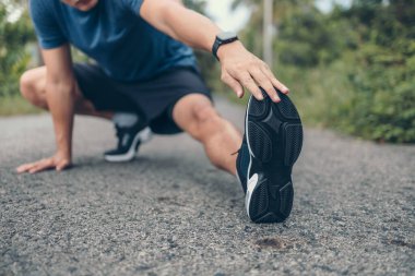 Genç adam koşmadan önce parkta geriniyor. Genç adam parktaki fitness antrenmanından önce antrenman yapıyor. Sağlıklı ve egzersiz yapan genç adam ormanda ısınıyor..