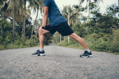 Genç adam koşmadan önce parkta geriniyor. Genç adam parktaki fitness antrenmanından önce antrenman yapıyor. Sağlıklı ve egzersiz yapan genç adam ormanda ısınıyor..