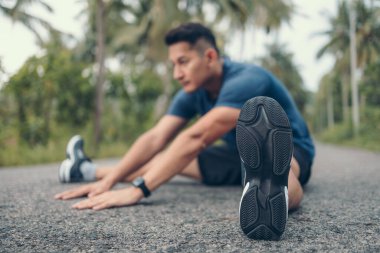 Genç adam koşmadan önce parkta geriniyor. Genç adam parktaki fitness antrenmanından önce antrenman yapıyor. Sağlıklı ve egzersiz yapan genç adam ormanda ısınıyor..