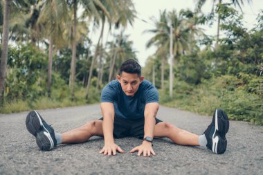 Genç adam koşmadan önce parkta geriniyor. Genç adam parktaki fitness antrenmanından önce antrenman yapıyor. Sağlıklı ve egzersiz yapan genç adam ormanda ısınıyor..