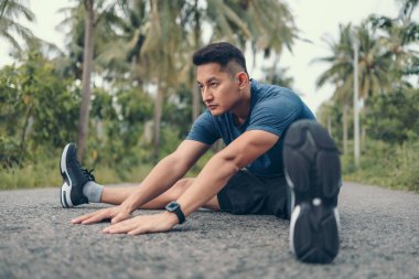 Genç adam koşmadan önce parkta geriniyor. Genç adam parktaki fitness antrenmanından önce antrenman yapıyor. Sağlıklı ve egzersiz yapan genç adam ormanda ısınıyor..