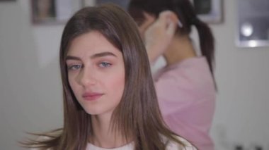 Kozmetik uzmanı müşterinin arkasından yürürken plastik kalkanı çıkarıyor.