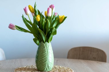 Nice composition of pink and yellow tulips inside a green vase on a wooden table. White background.