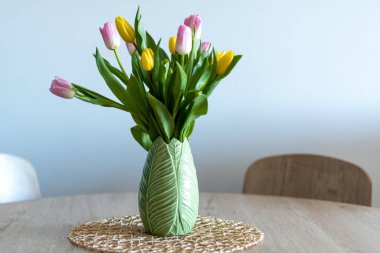Nice composition of pink and yellow tulips inside a green vase on a wooden table.