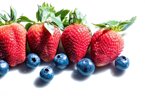 Four Very Red Strawberries Several Blueberries White Background 免版税图库照片