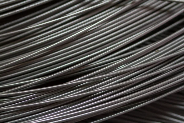 Stainless steel wire in production workshop or construction site. Close-up of wire rollers for spring production or concrete reinforcement. Metal texture. Industrial or construction concept.