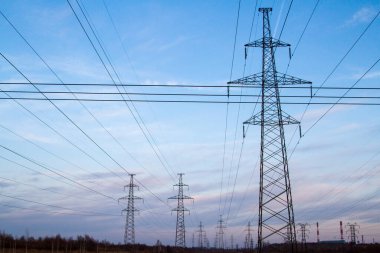Gün batımında bir alanın ortasında yüksek voltajlı elektrik hatları. Sanayileşme. Elektrik şoku. Güç arzı.
