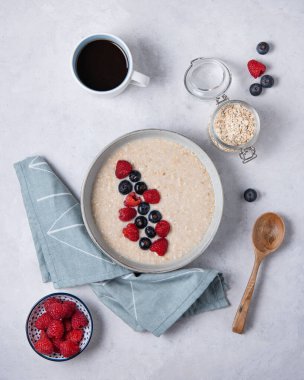 Yulaf ezmeli yulaf lapası, yaban mersini ve ahududulu gri bir kasede. Sağlıklı kahvaltı, diyet, vejetaryen yemeği ve bir fincan kahve. Üst görünüm