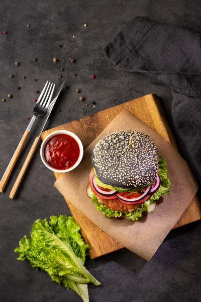 Healthy vegetarian black burger with vegetables ant tomato souce on a cutting Board on a dark background. Top view and copy space