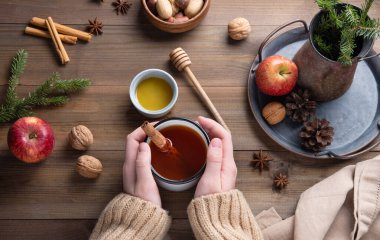 Eller aromalı Noel Elması çayını ahşap bir masada tarçınlı tutuyor. Üst görünüm