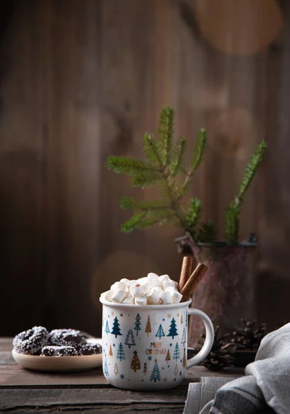 Christmas cup of cacao and marshmallow with cinnamon on an old brown wooden table with cookies, bokeh, cones and fir. New year mood. Front view and copy space