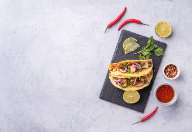 Tavuklu, soğanlı, biberli, mısırlı ve fasulyeli iki Meksika sokak tacosu limon dilimi ve baharatla servis edilen bir karatahtanın üzerinde çekiliyor. Üst görünüm ve kopyalama alanı