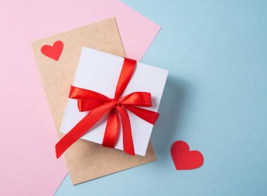 Tam bir kutlama havası. Pastel pembe ve mavi arka planda beyaz hediye kutusu ve el işi zarfı. Sevgililer Günü konsepti, Anneler Günü, düğün günü. Üst görünüm