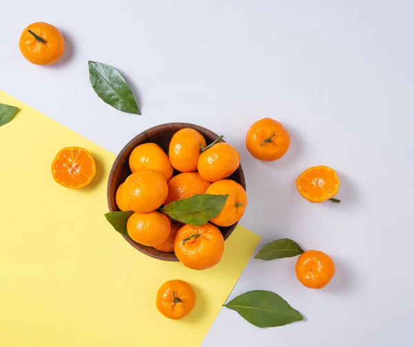 甜甜的 多汁的橘子 绿色的叶子在一个木制碗在一个时髦的黄灰色背景 顶部视图和复制空间 — 图库照片
