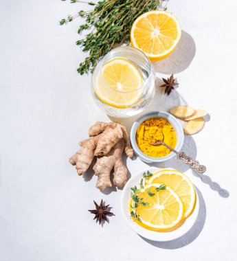  Zerdeçal, kekik, limon, yıldız anason ve beyaz arka planda sert gölgeli limonlu cam su malzemeleriyle bembeyaz yatıyordu. Üst görünüm, alanı kopyala