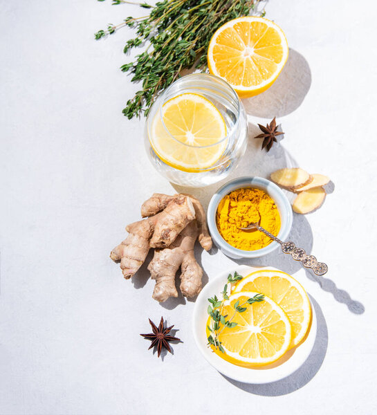  Плоский лежал с ингредиентами из куркумы, тимьяна, лемона, звездного аниса и стеклянной воды с лемоном на белом фоне с твердыми тенями. Вид сверху, пространство для копирования