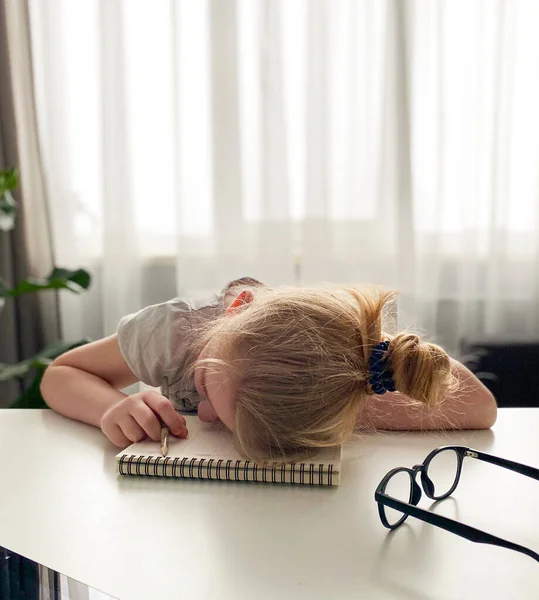 the schoolgirl was tired of home schooling and fell asleep at the table on a notebook with a pencil in her hand . Distance learning during the coronavirus.