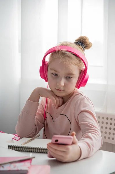 Distance education. A schoolgirl in pink headphones studying homework during their online lesson at home via the Internet. Social distance during quarantin