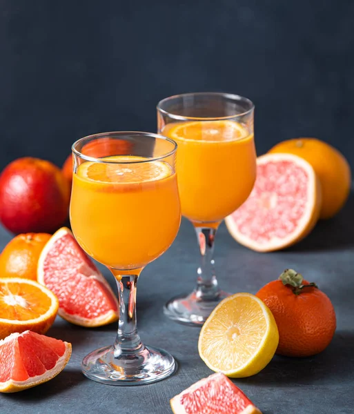 濃い灰色の背景に2つのガラスと新鮮な果物みかん オレンジ グレープフルーツ レモンの柑橘類のジュース 正面図 — ストック写真